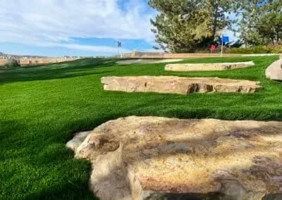 Large, light-colored landscape rocks set into a vibrant green lawn with trees and a blue sky in the background.