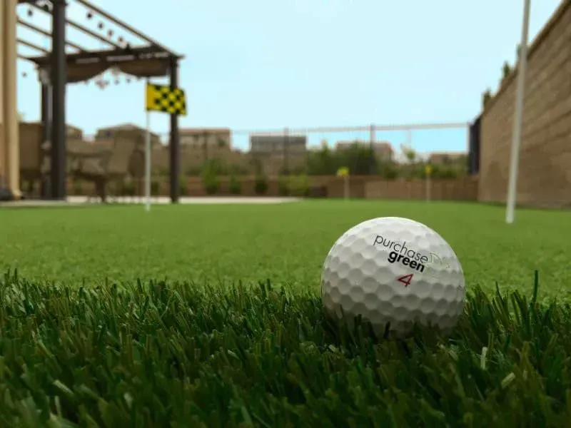 A golf ball resting on artificial putting green grass, with a checkered flag and pergola visible in the background.
