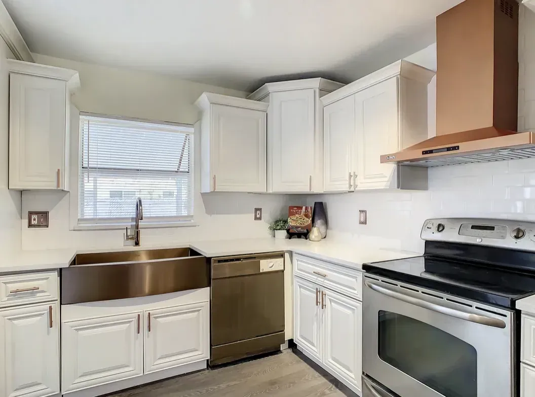 A bright kitchen featuring white cabinets, stainless steel appliances, a farmhouse sink, and a light-colored countertop.