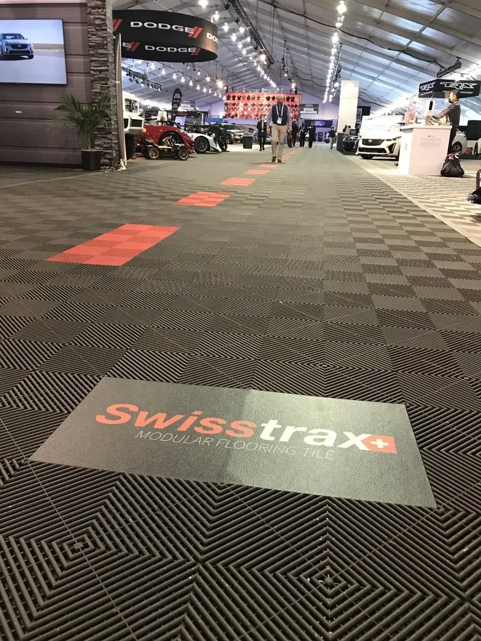 A long aisle covered in dark, textured modular flooring featuring a Swisstrax logo and red directional floor markings.