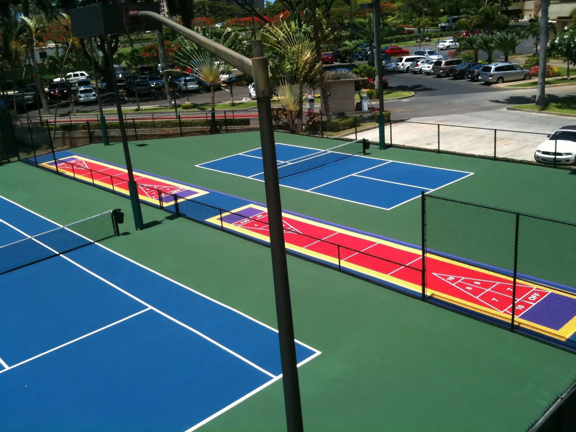 An outdoor facility featuring blue pickleball or tennis courts and red shuffleboard lanes on a green surface.