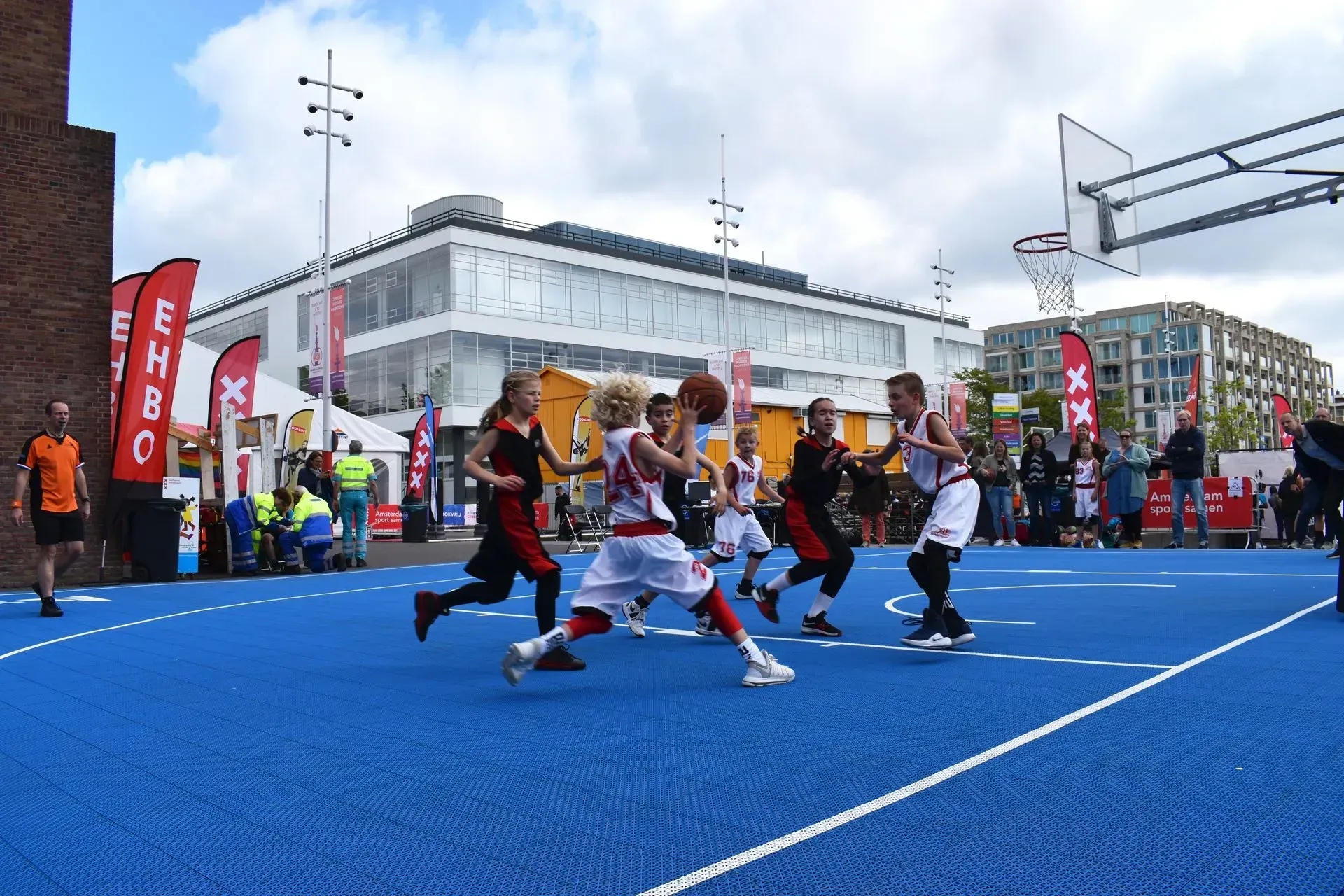 Children playing basketball on a blue court during an outdoor event.