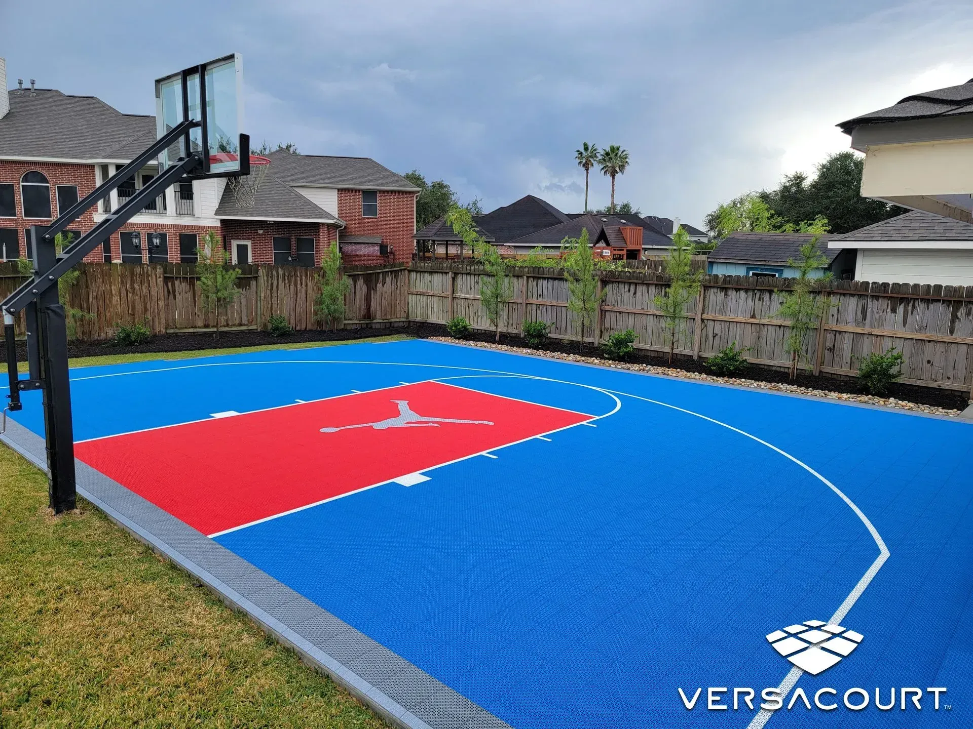 An outdoor blue and red basketball court with a Jordan logo, installed in a residential backyard.