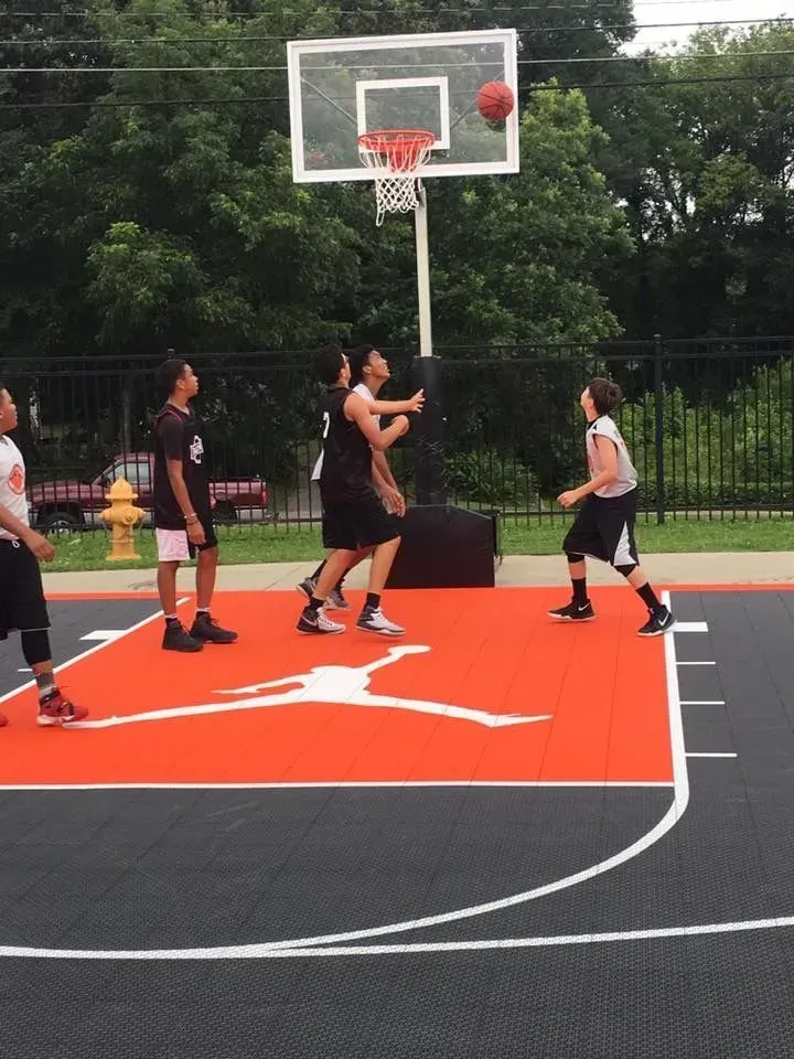 Four people playing basketball on an outdoor court with a red, Jordan-logo-branded key area and a black perimeter.