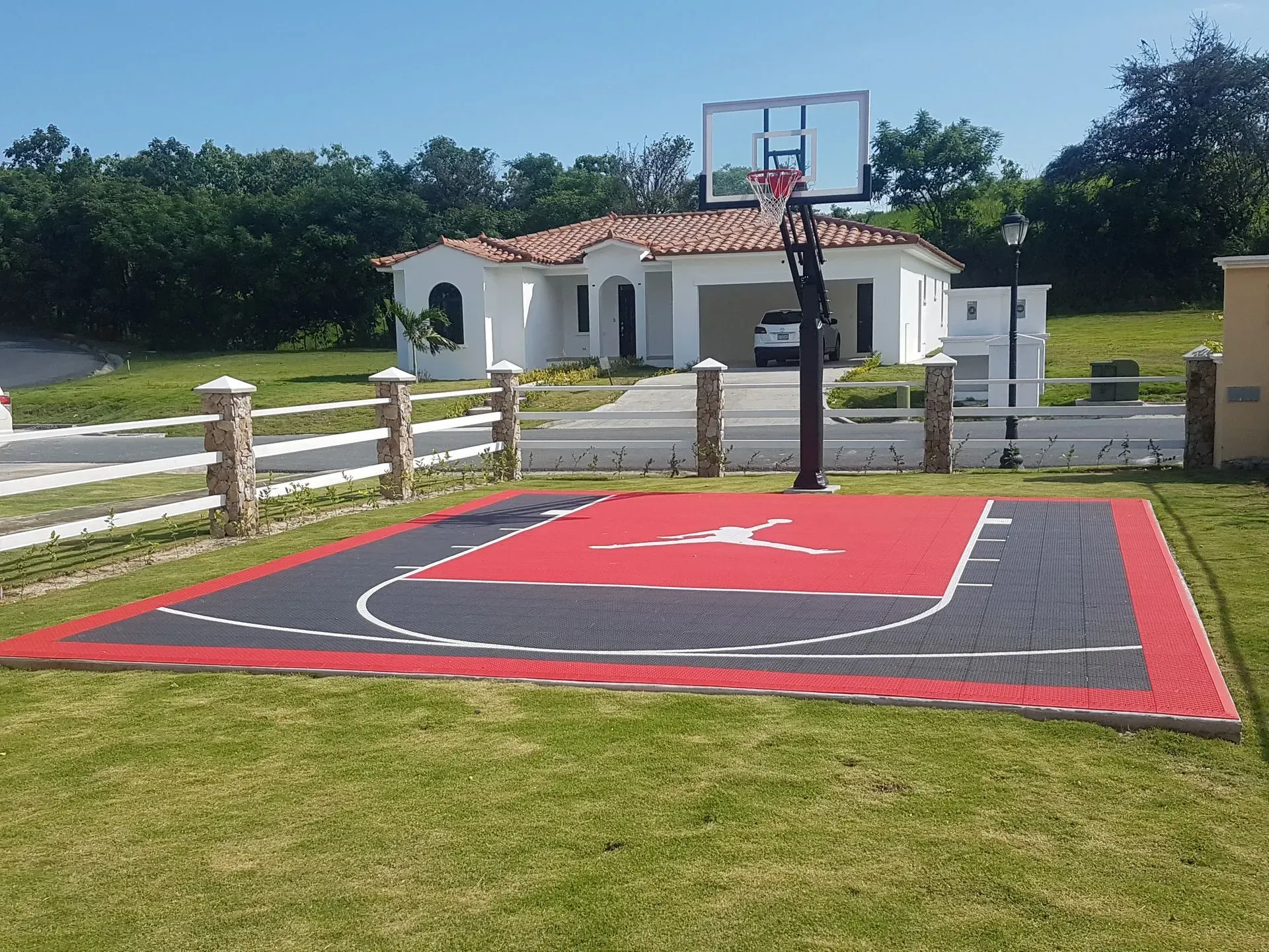 A Jordan-branded red and grey basketball court installed on a green lawn in front of a white house.