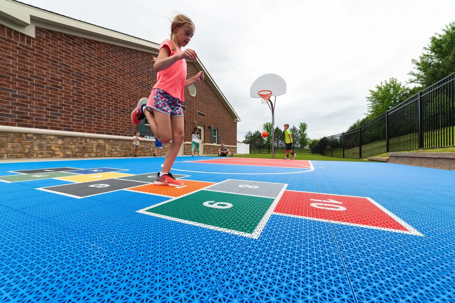 A child plays hopscotch on a bright blue outdoor court near a brick building.
