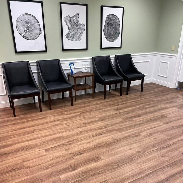 A waiting room with wooden floors and black chairs