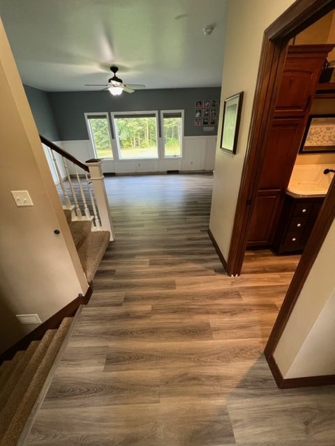A hallway with hardwood floors leading to a bathroom and stairs