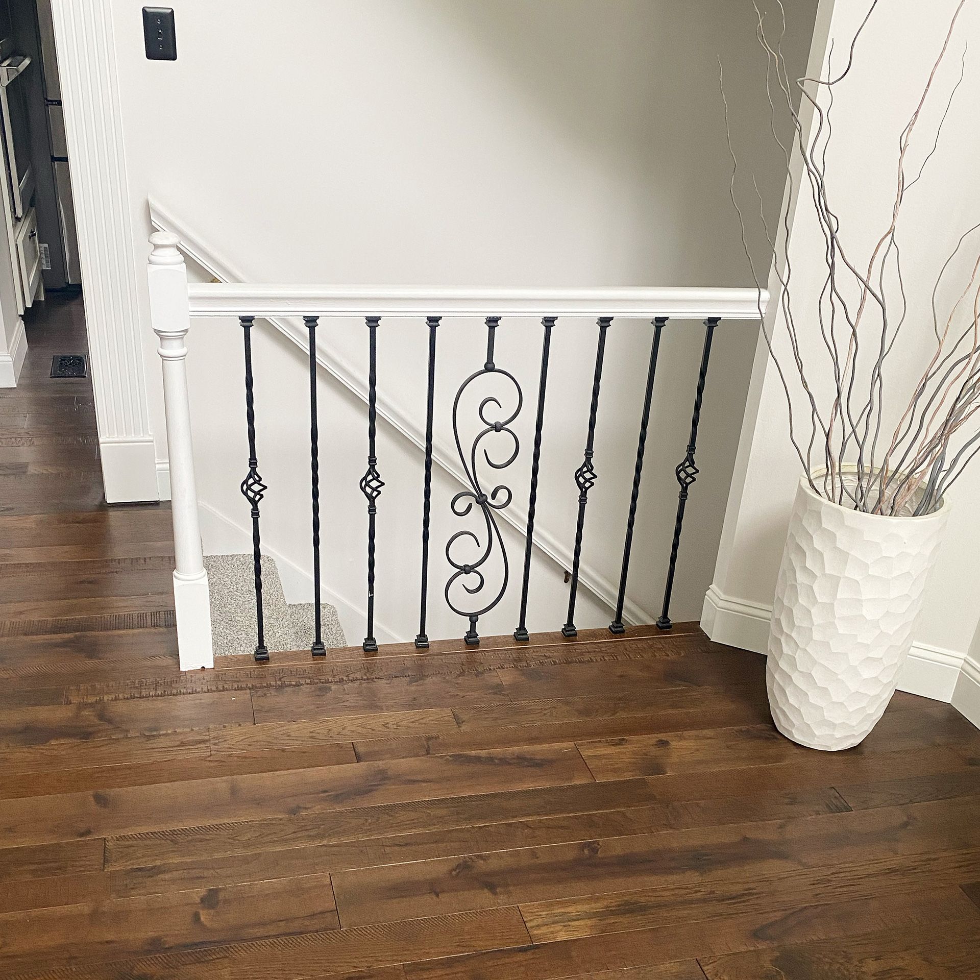 A staircase with a white railing and a white vase on the hardwood floor