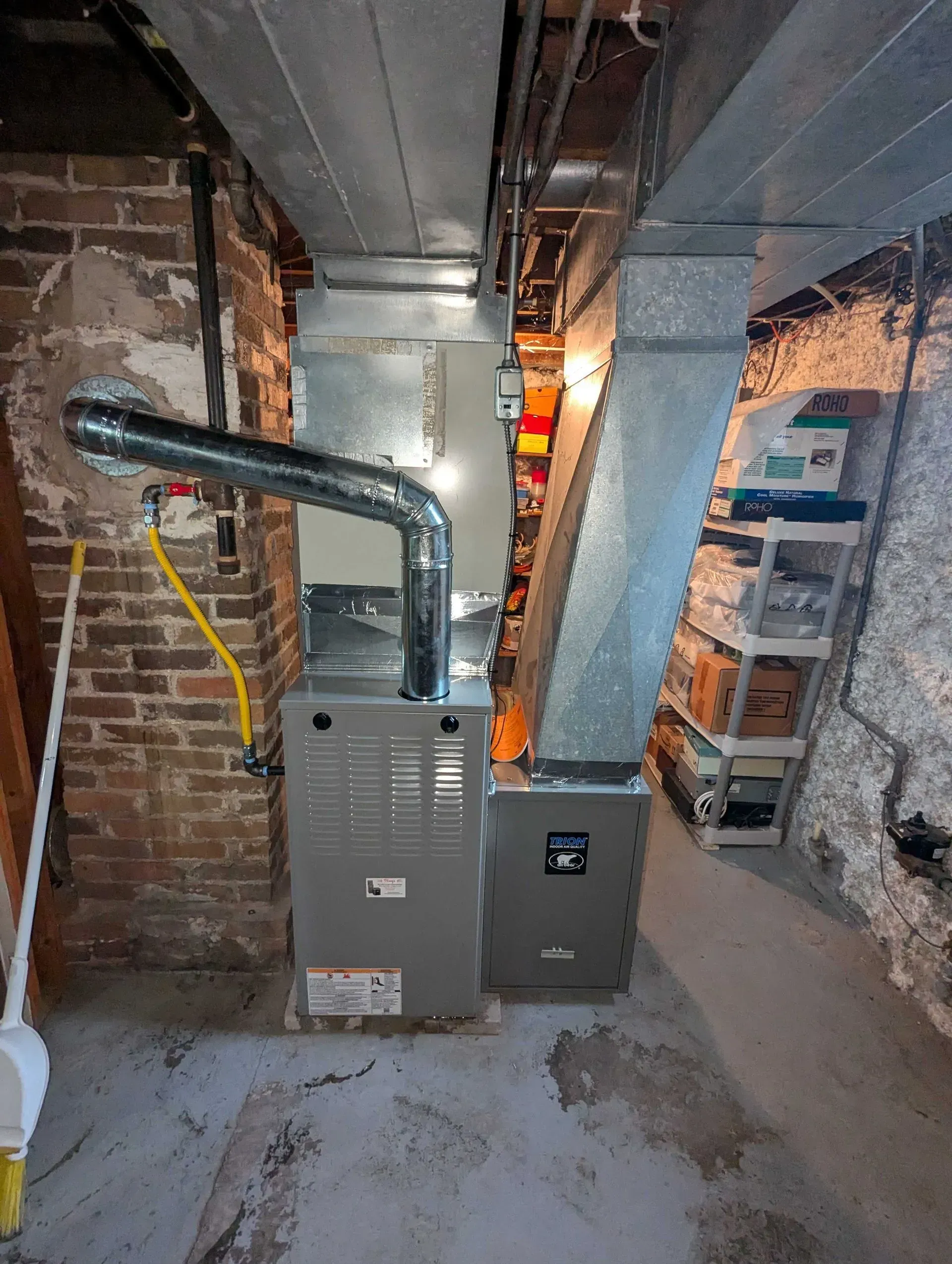 Basement furnace and metal ductwork beside exposed brick and pipes in a utility room