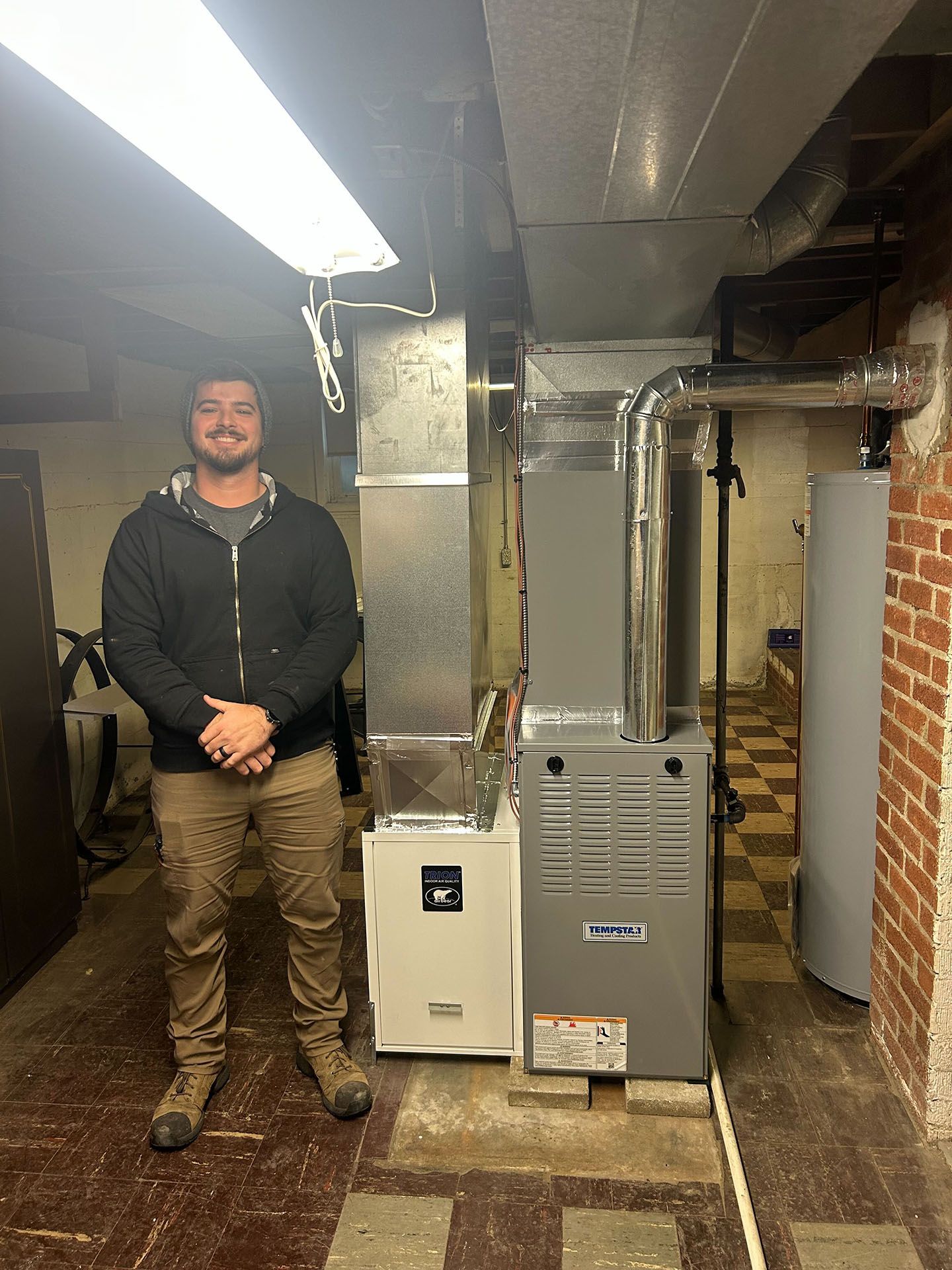 Man stands next to new furnace and ductwork in a basement.