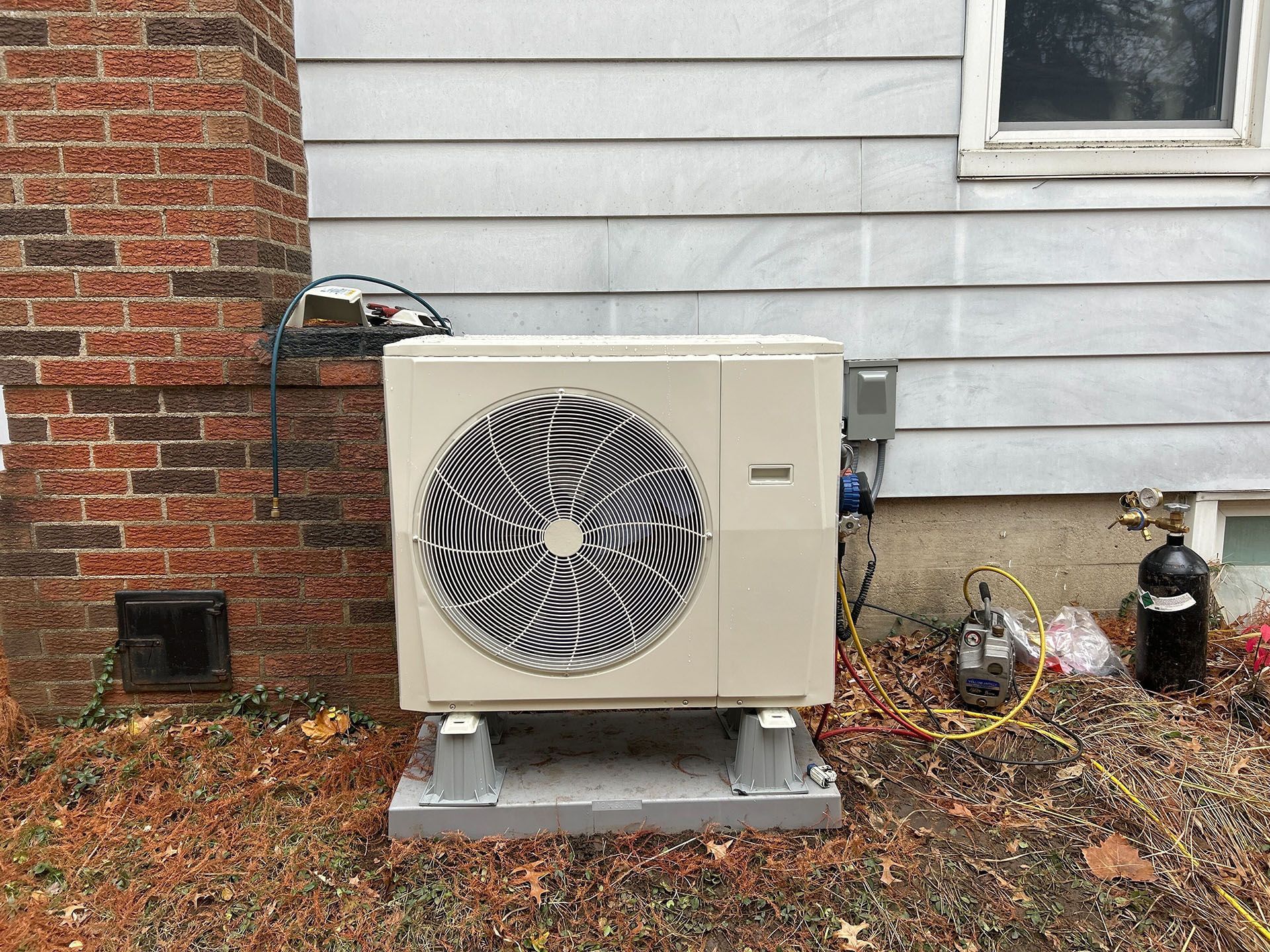An outdoor air conditioning unit on a concrete base next to a house and brick chimney.