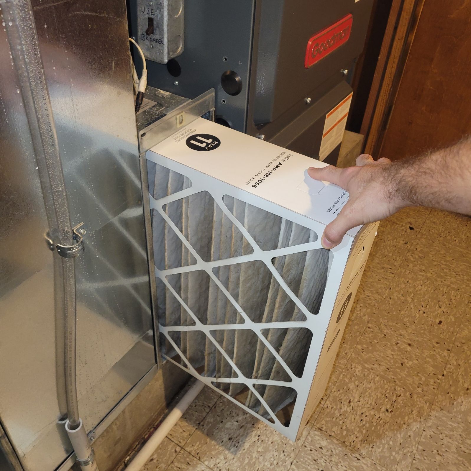A person removing a new air filter from a furnace in a basement.