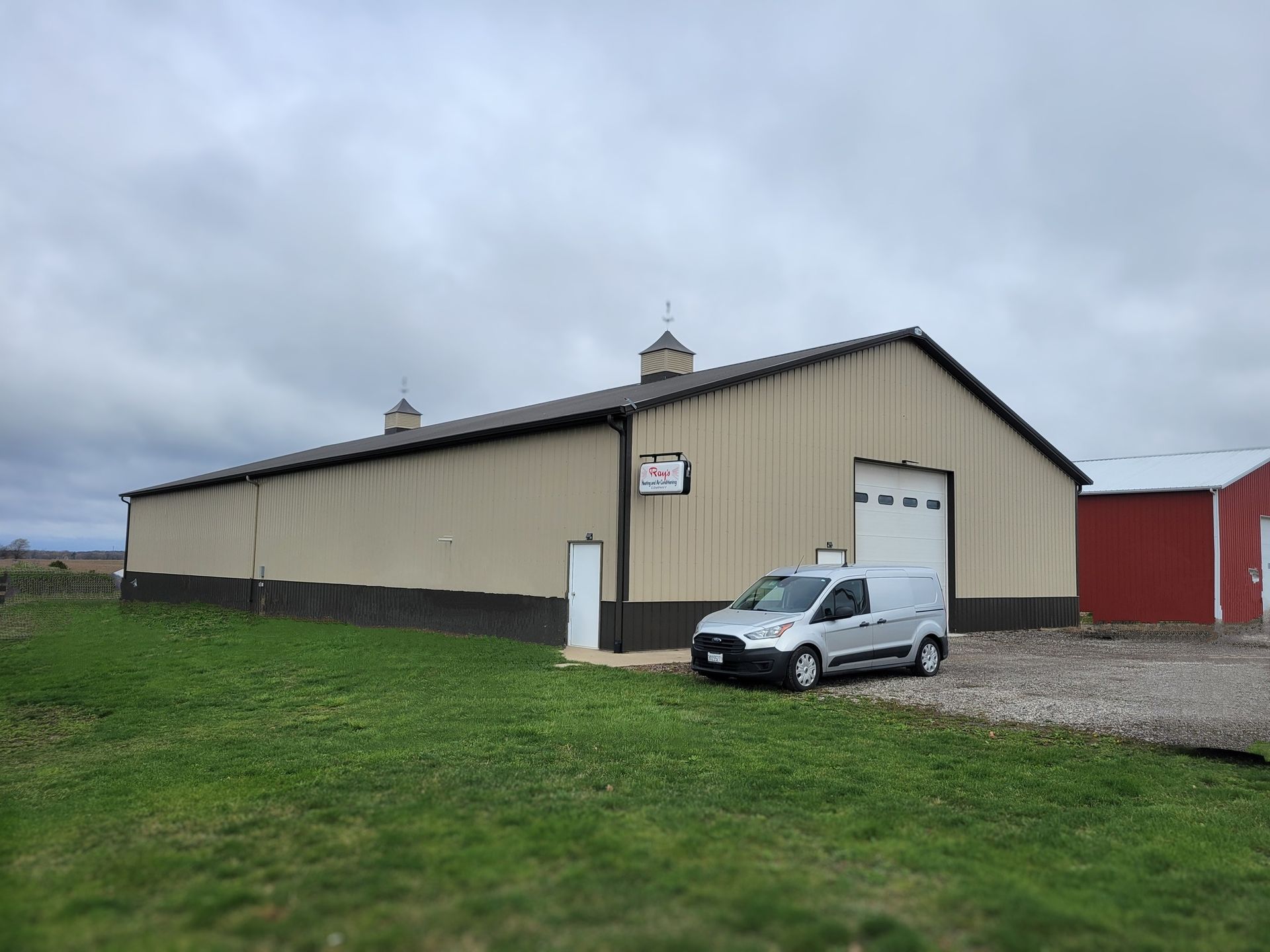 A large tan metal building with a garage door; a white van parked outside on a cloudy day.
