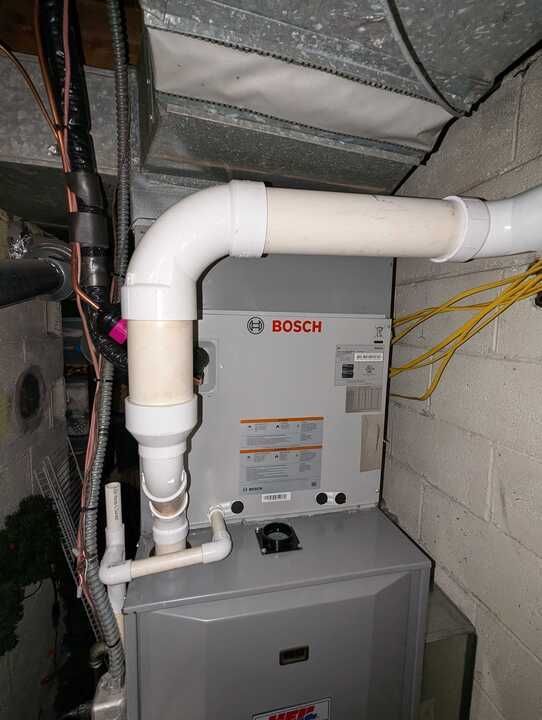 A Bosch furnace with white PVC pipes in a basement setting.