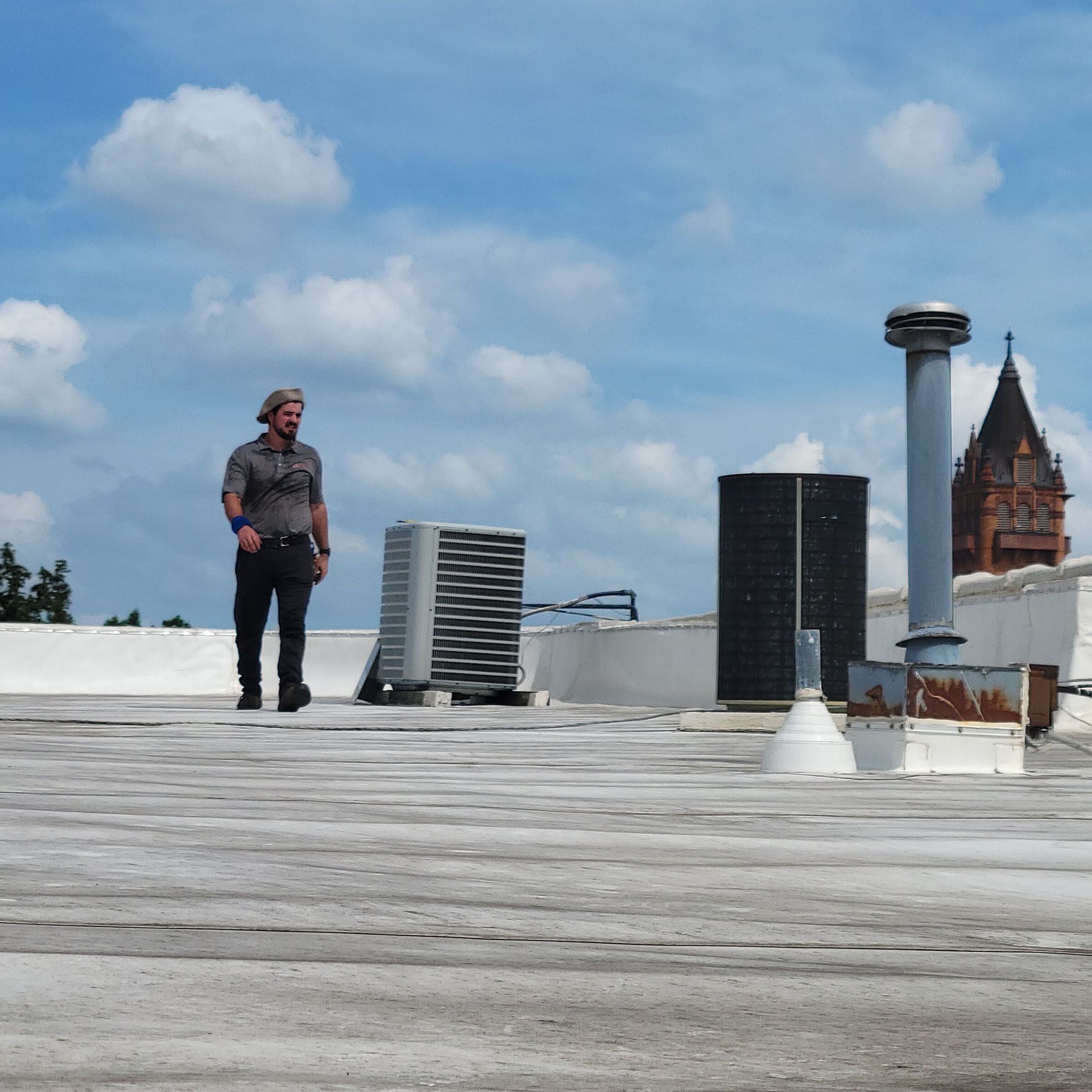 Man with grey hair on a rooftop with air conditioning units, chimney and building with a steeple in the background.