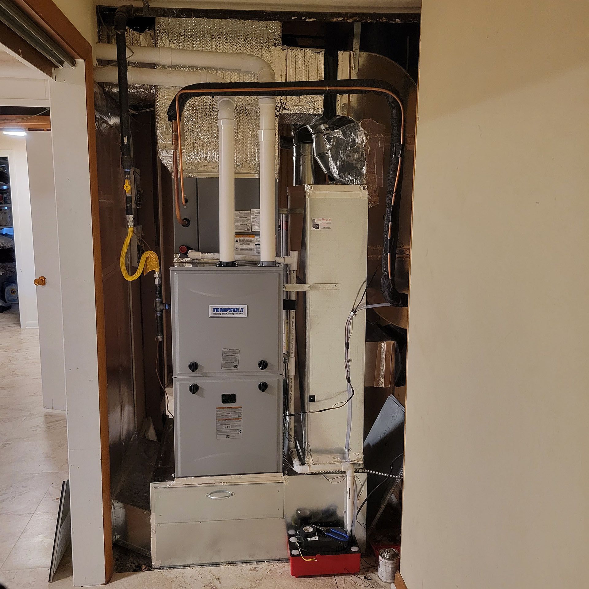 Furnace and air handler in a wall opening, surrounded by ductwork and insulation.