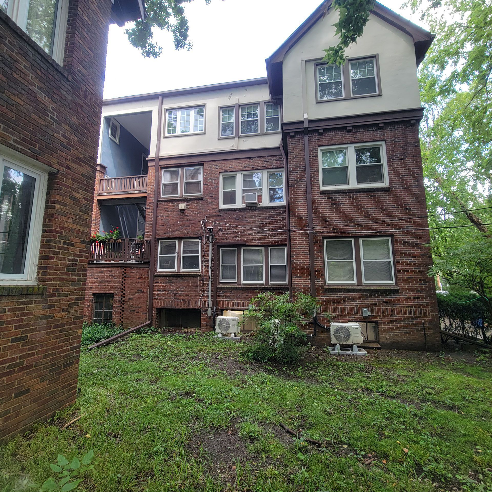 Back exterior of a brick apartment building with multiple windows, a small yard, and overgrown grass.