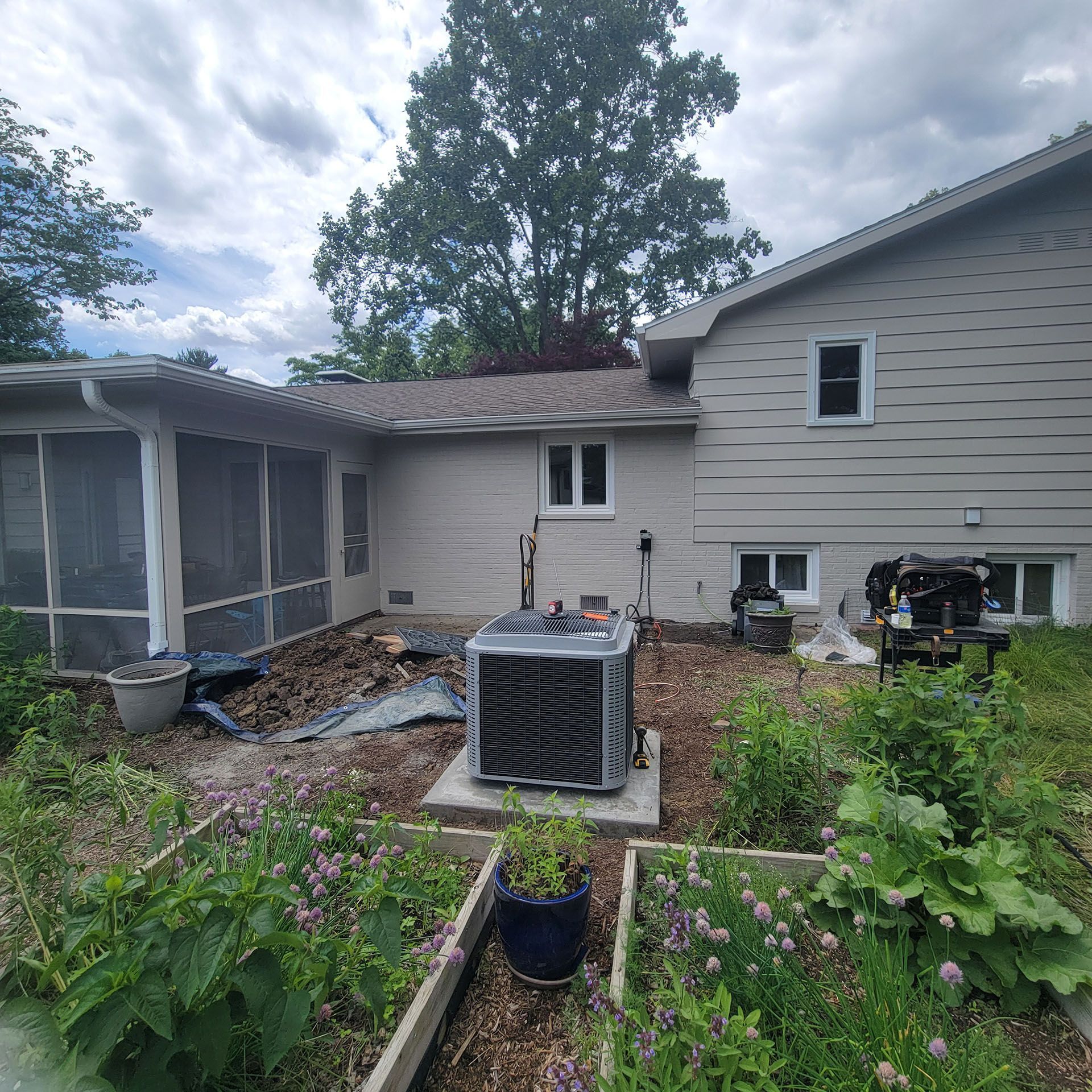 Backyard with a house, screened porch, garden beds, and an air conditioning unit. Overcast sky.