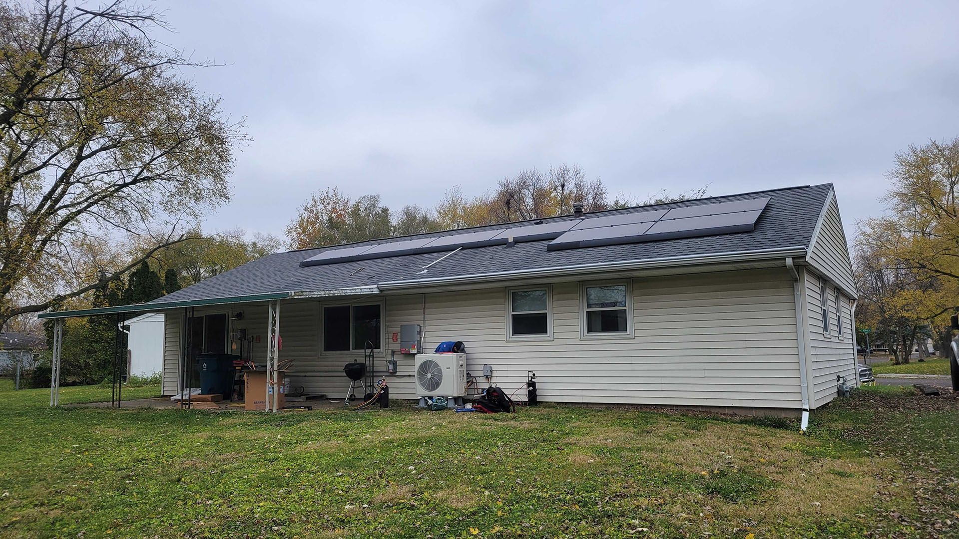 A white house with solar panels on the roof under a cloudy sky, with grass in the foreground.