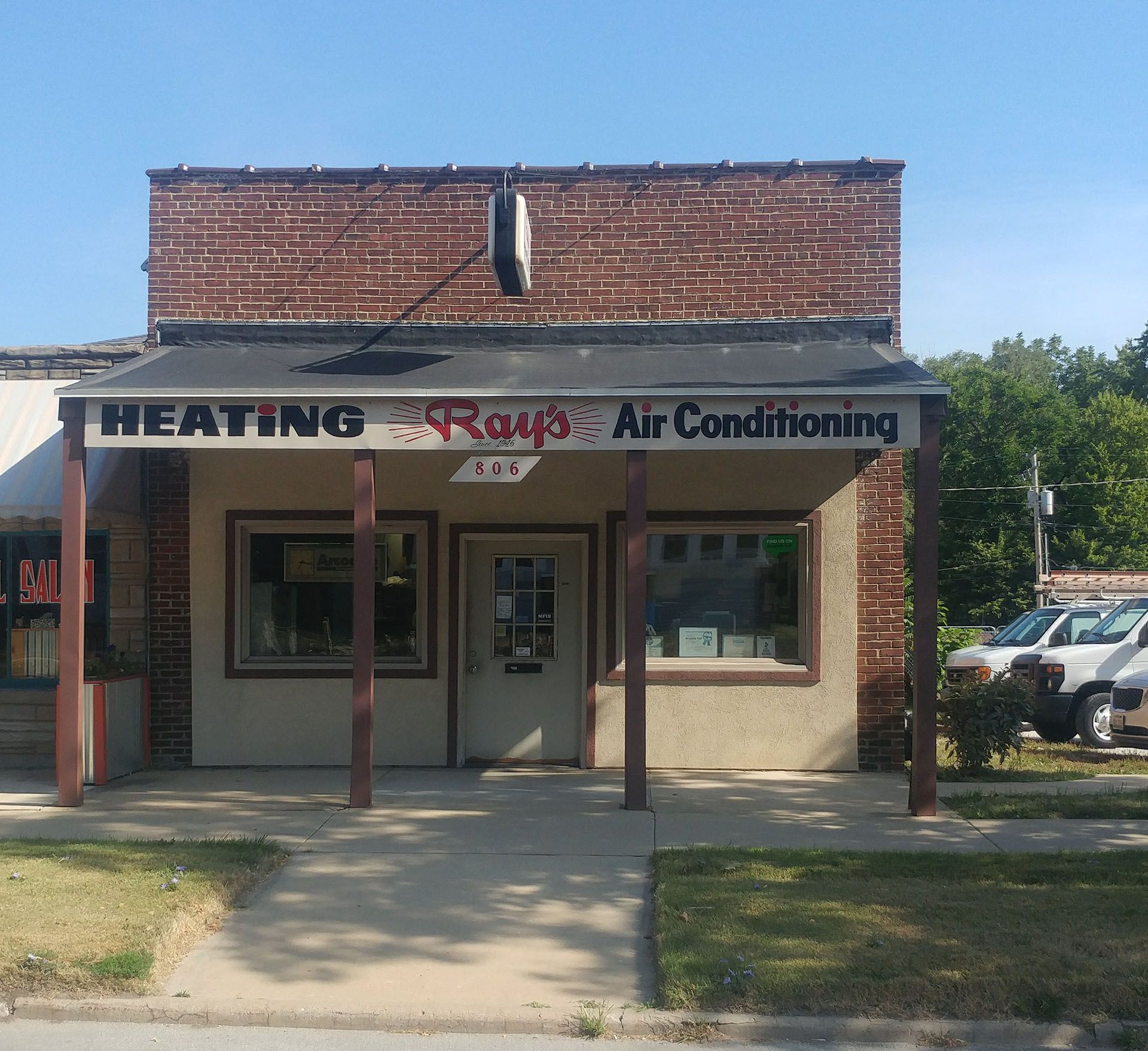 Ray's Heating & Air Conditioning building with awning, beige walls, brick facade, and parked service vehicles.