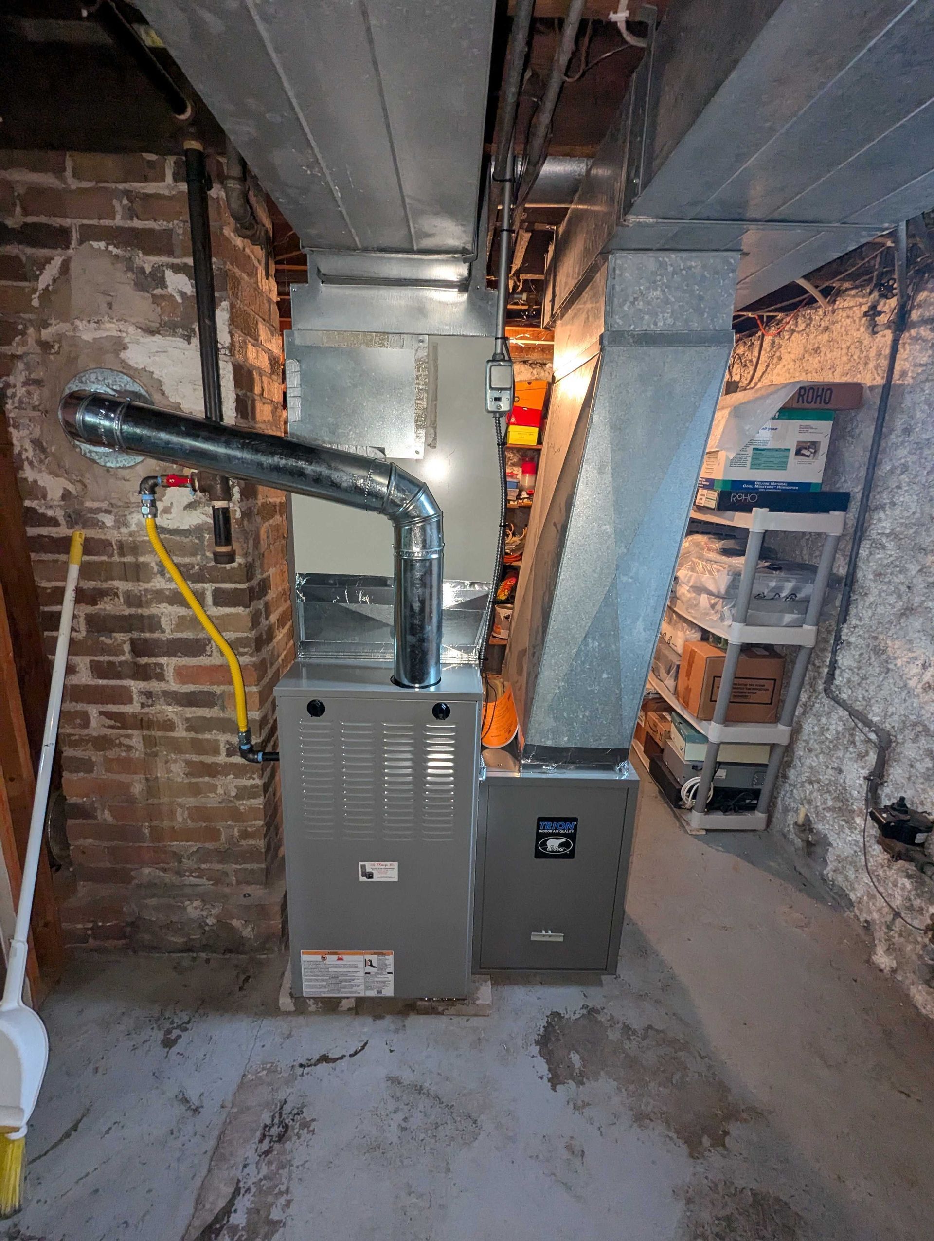 Furnace in a basement, with silver ductwork and brick walls.
