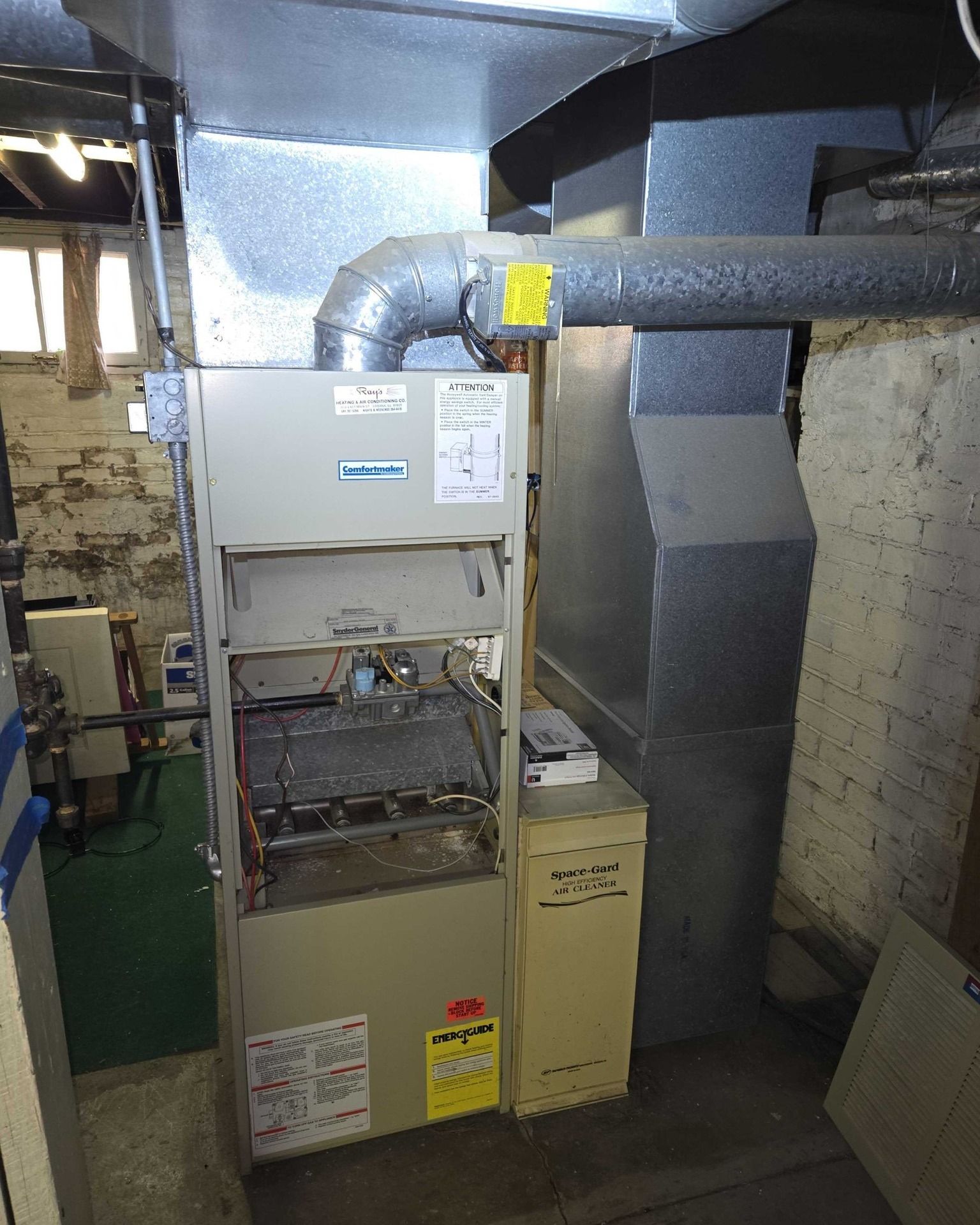 Furnace in a basement with ductwork, attached to a brick wall.