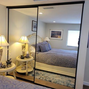A bedroom with a bed, nightstand, lamp, and a large mirror