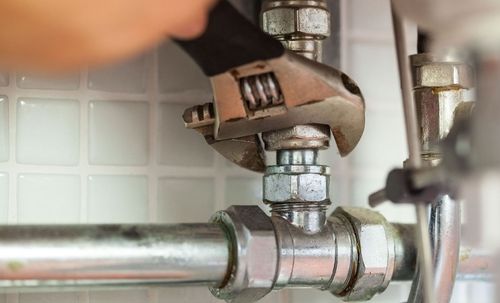 A person is fixing a pipe with a wrench.