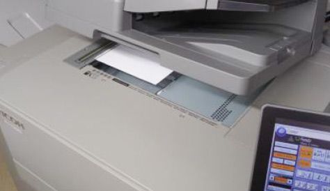 A printer is scanning a piece of paper next to a monitor.