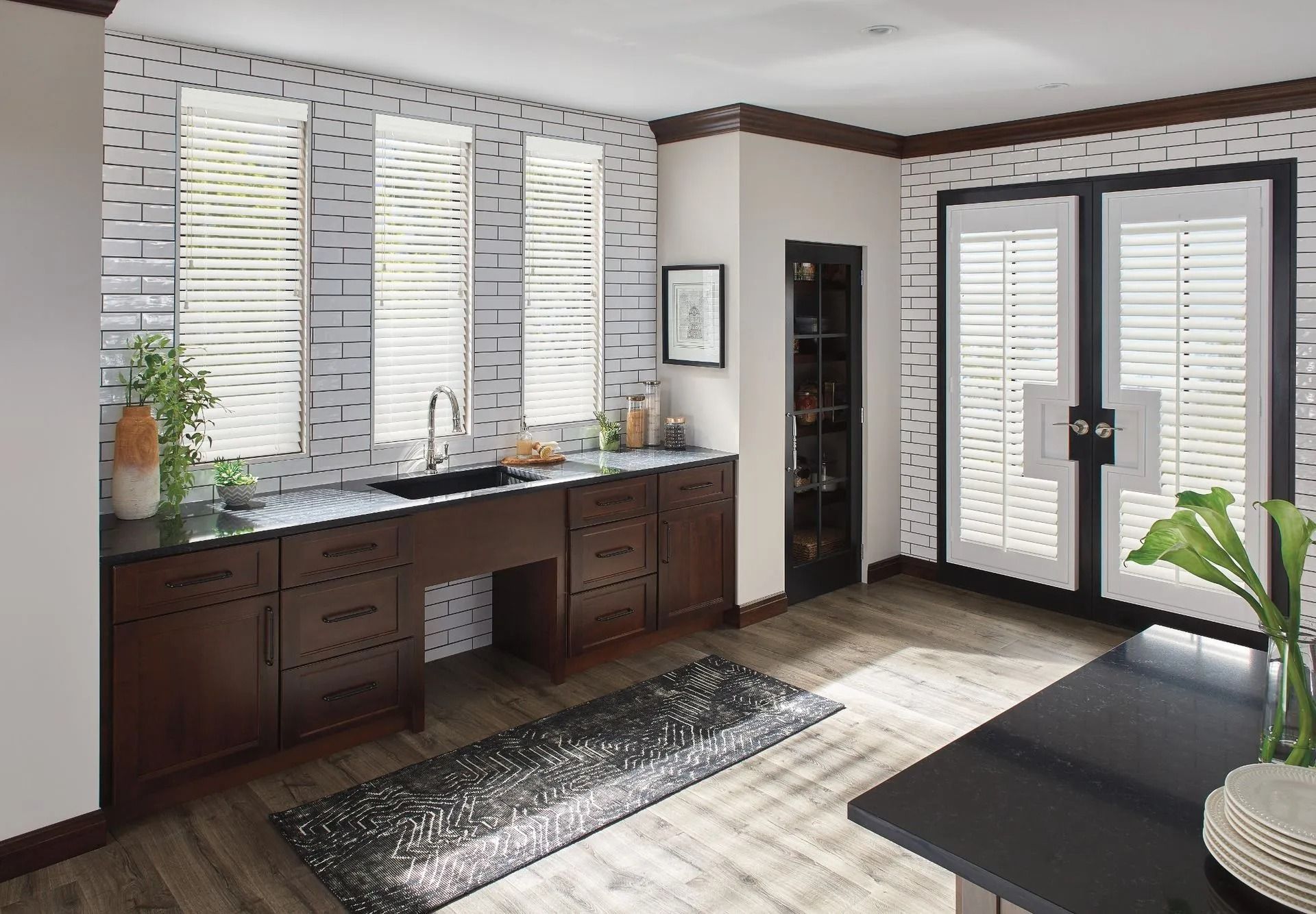 A modern kitchen features dark wood cabinets, a black sink, patterned brick backsplash, and double glass doors.