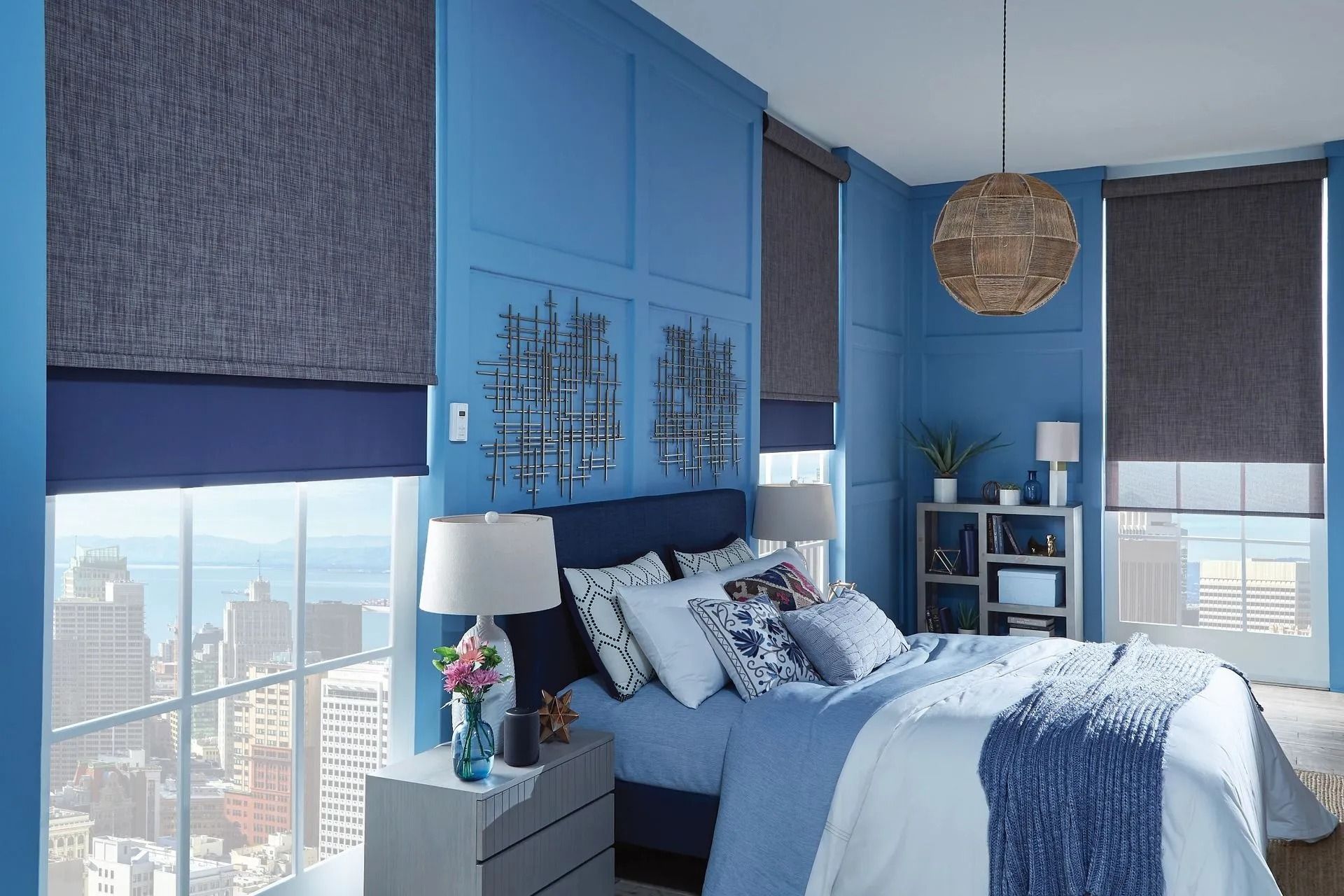 Bedroom with blue walls, a bed, gray roller shades on windows, and city views.