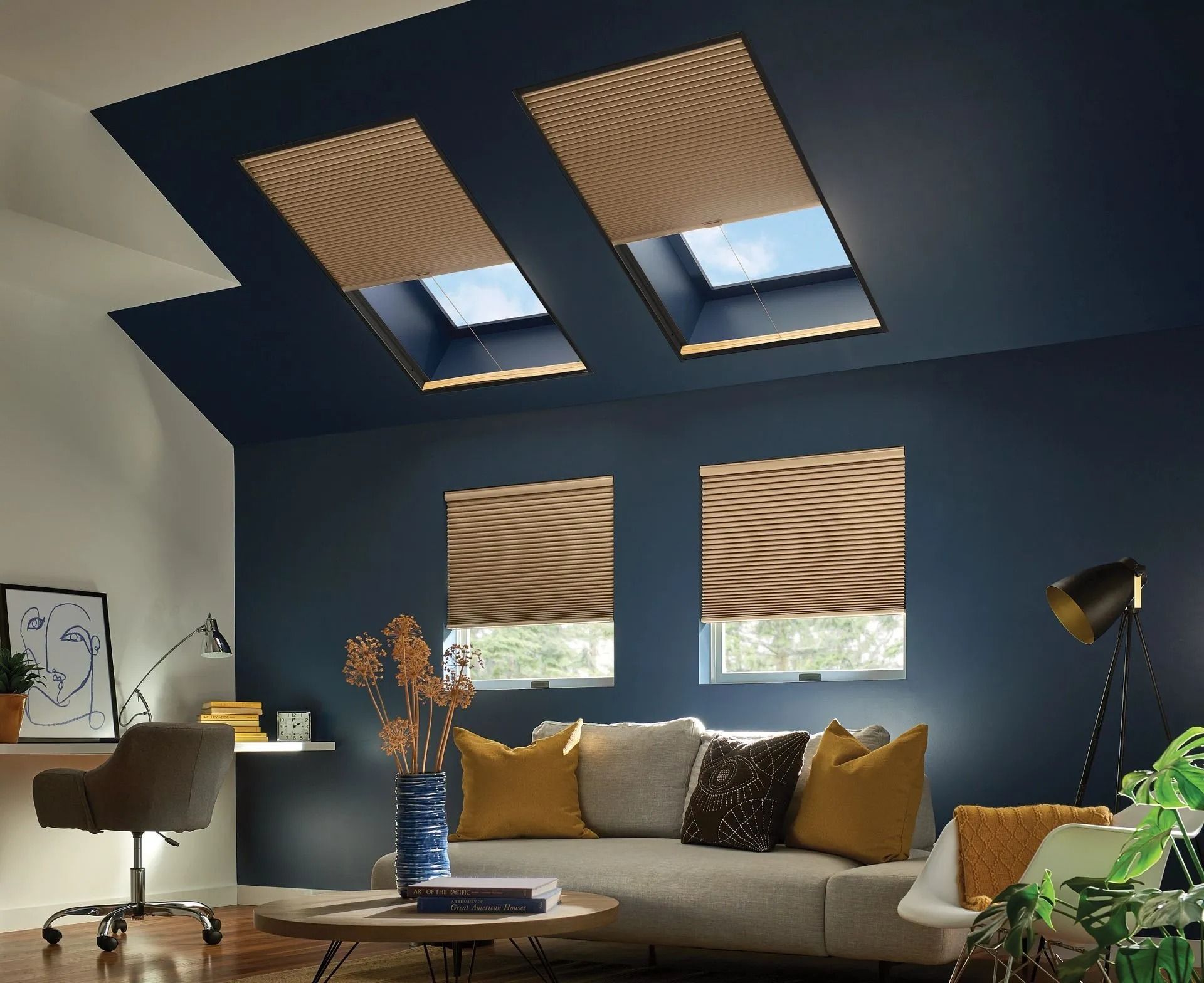 A modern living room with deep blue walls, a light sofa with yellow pillows, two skylights, and two windows with tan shades.