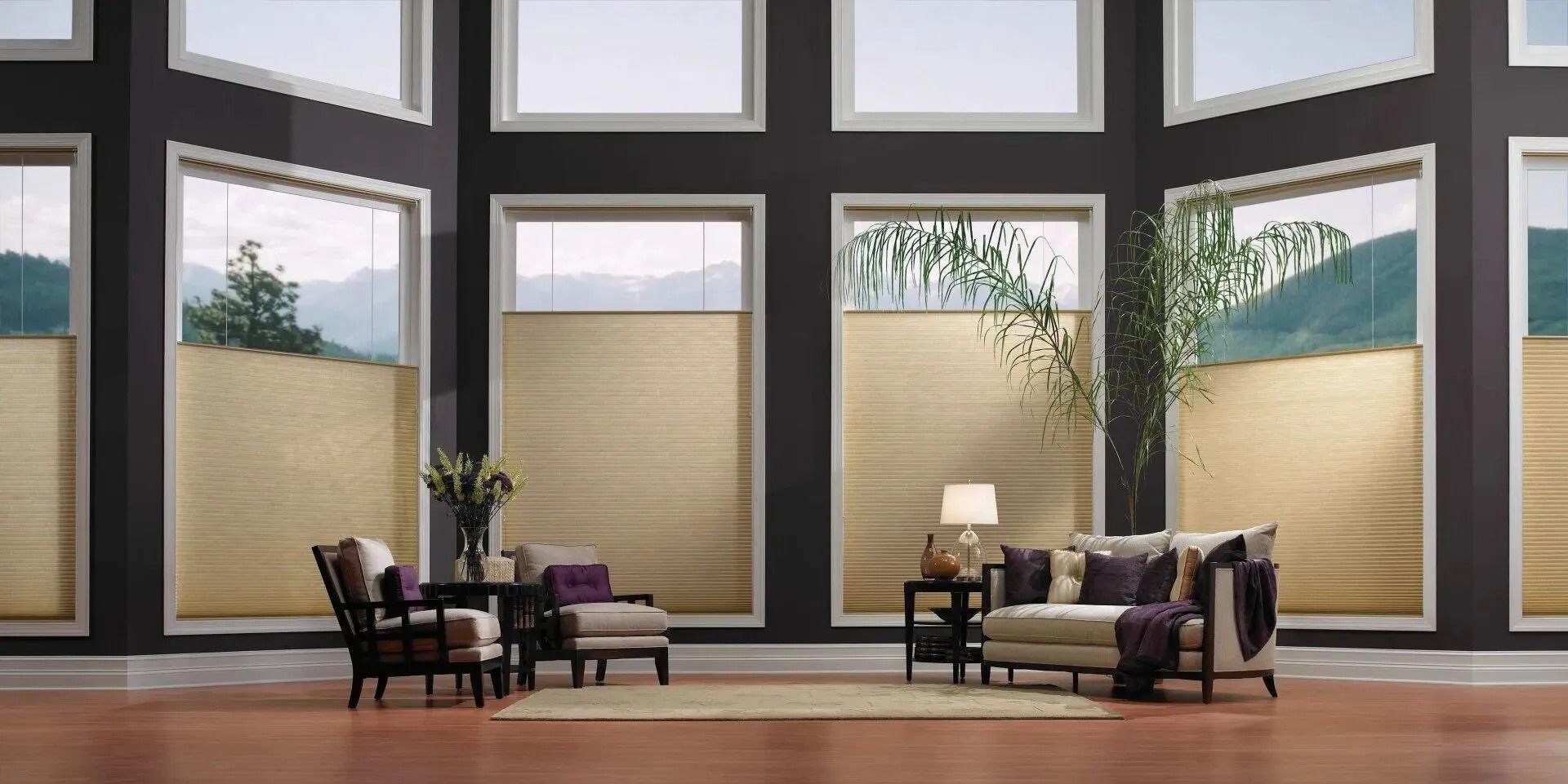 Living room with large windows, tan cellular shades, dark walls, two chairs, a sofa, and a table with a lamp.
