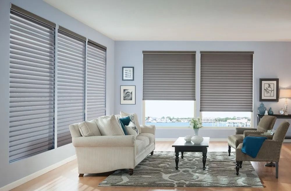 A living room featuring light blue walls, a cream sofa, a coffee table, and windows covered with gray pleated blinds.