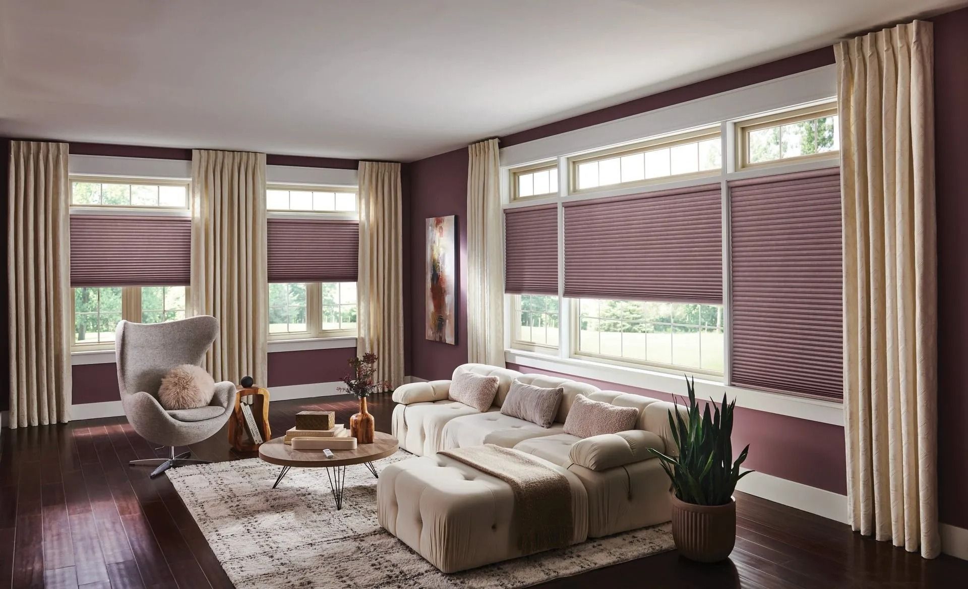 Modern living room with deep plum walls, a beige sectional sofa, a grey lounge chair, and tiered roman shades on windows.