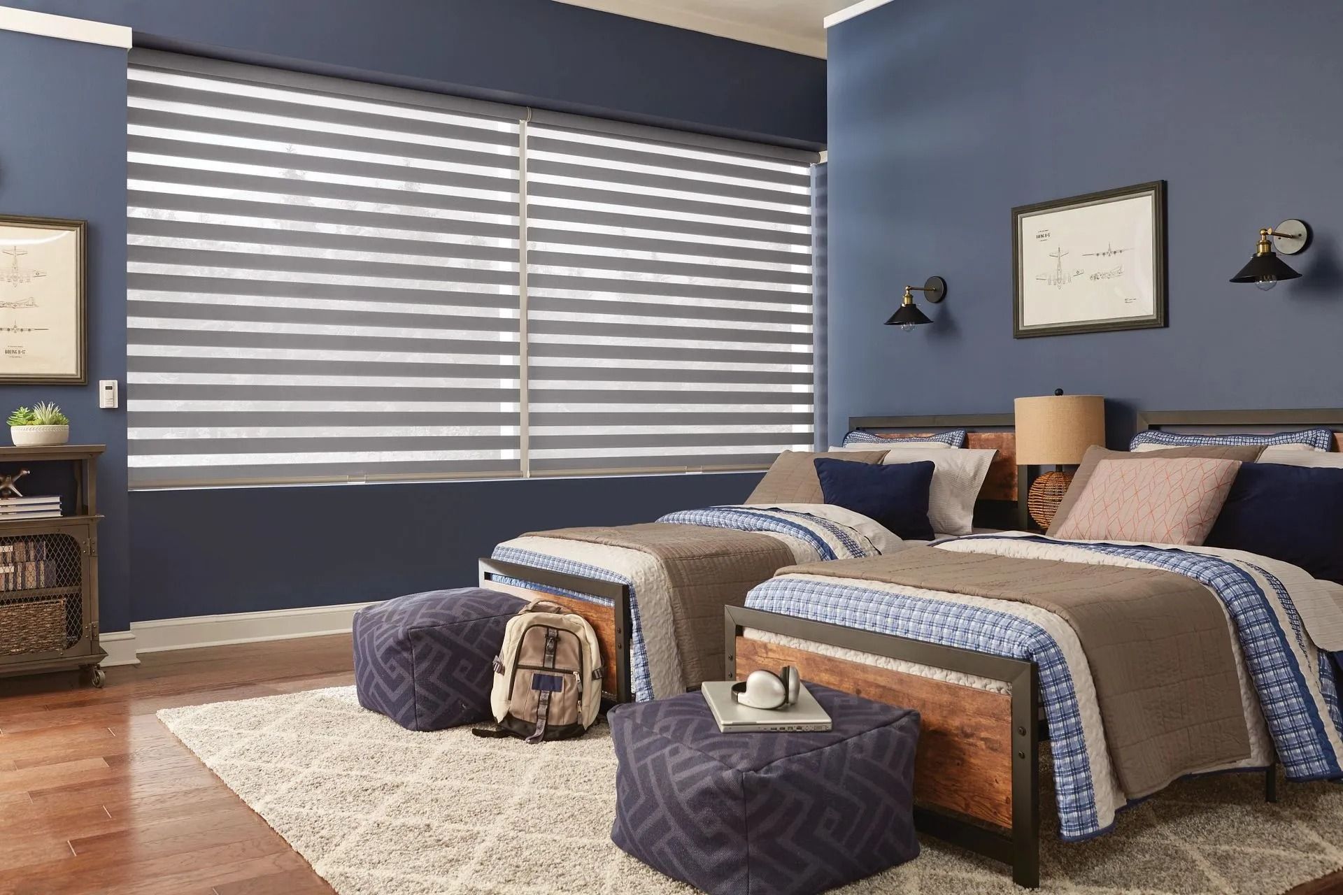 A modern bedroom with blue walls, two twin beds, patterned bedding, dark ottomans, and horizontal window shades.