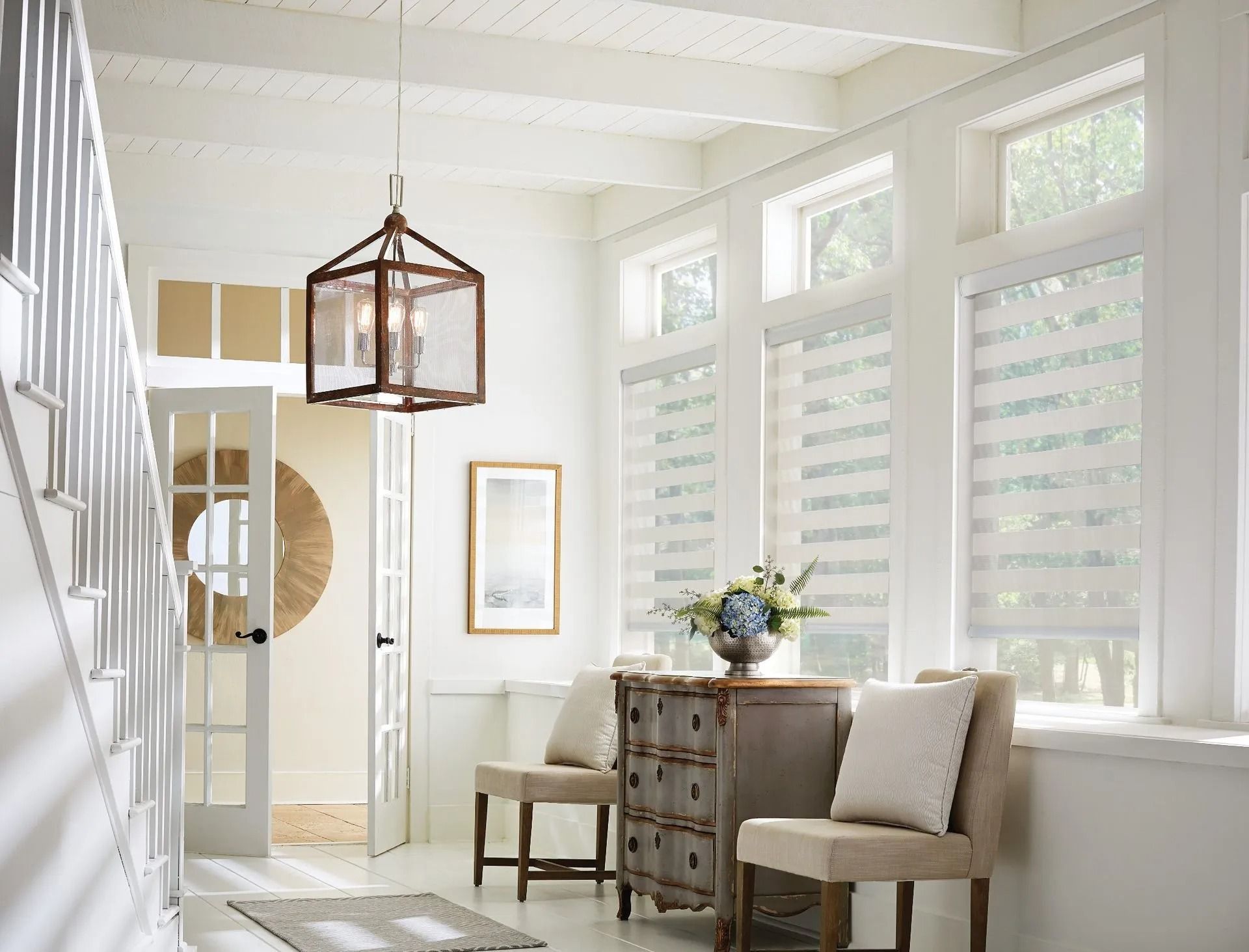 Bright entryway with a wooden lantern pendant light, white walls, striped shades on tall windows, and a small dresser.