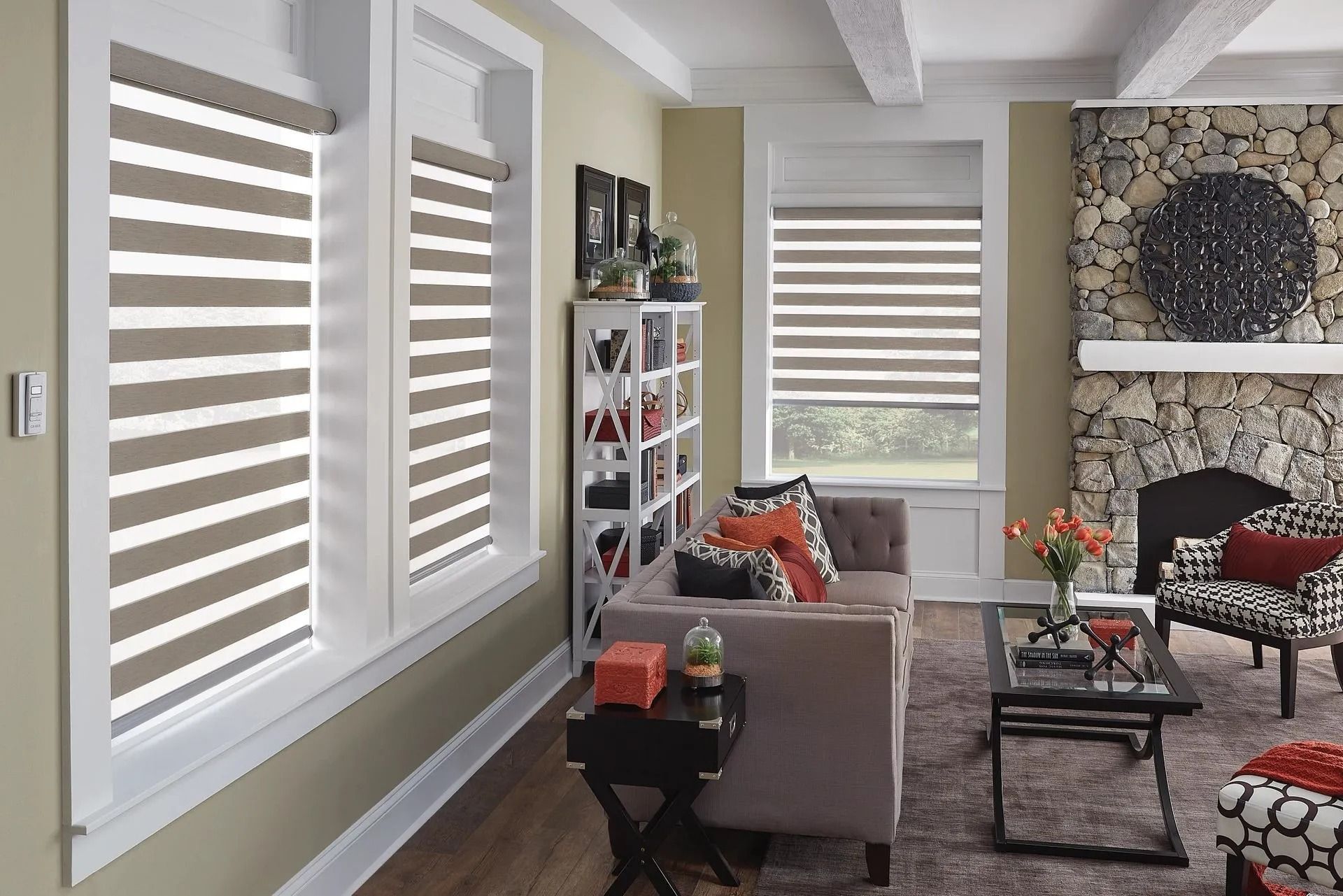 A cozy living room with striped roller shades on windows, a sofa, a stone fireplace, and patterned furniture.