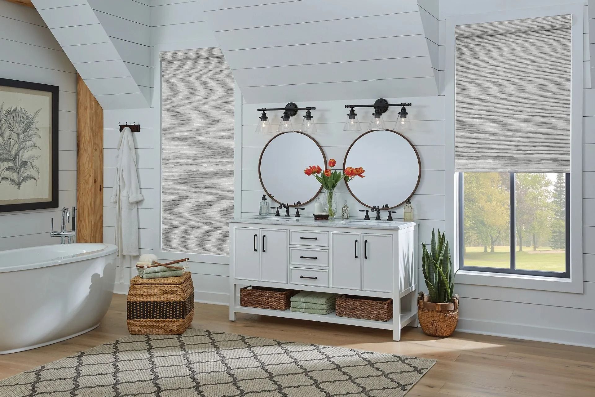 A modern farmhouse bathroom with a double vanity, circular mirrors, a white soaking tub, and patterned window shades.