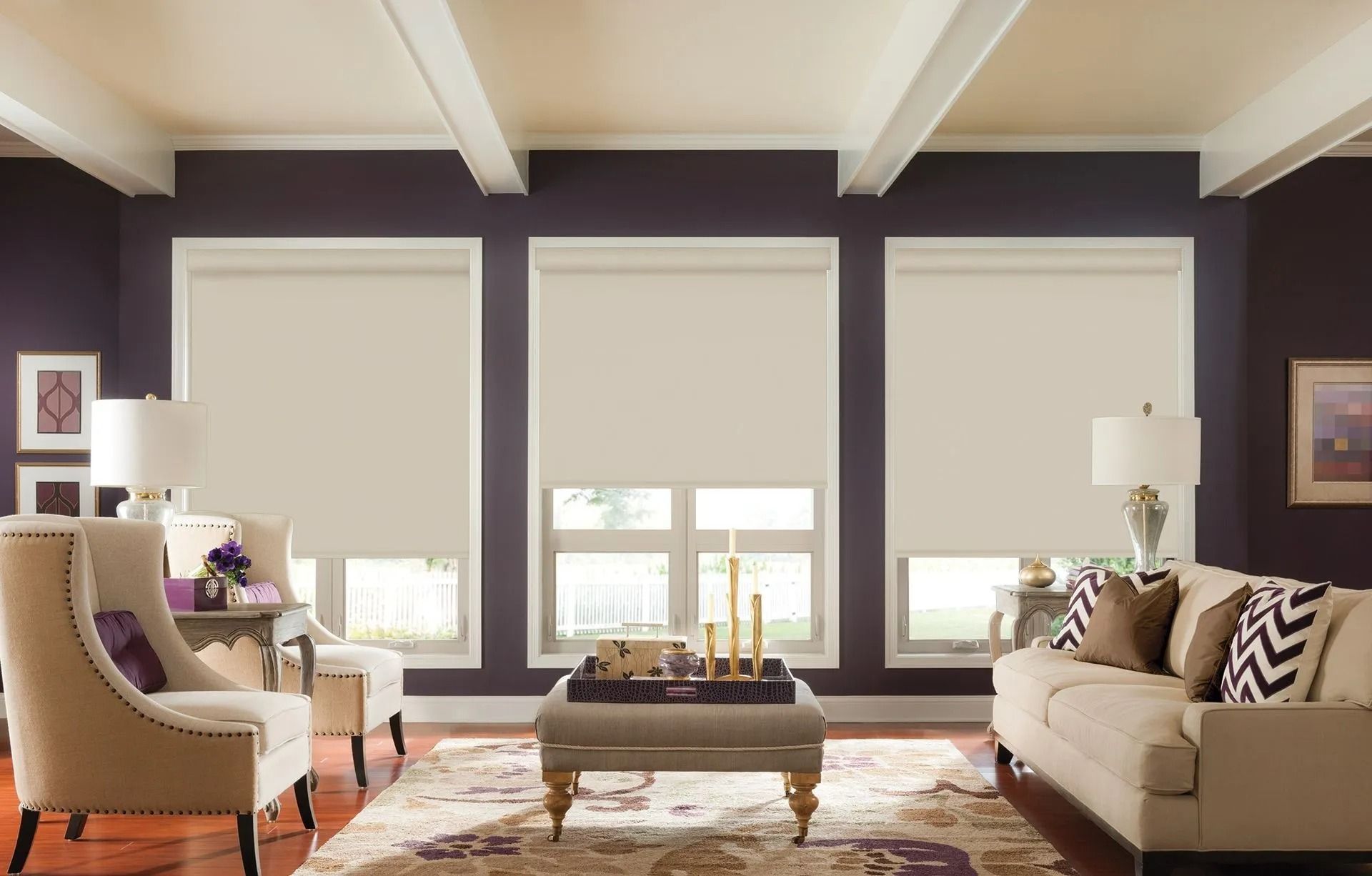 A living room with three windows featuring light-colored roller shades, an armchair, a couch, and a center ottoman.
