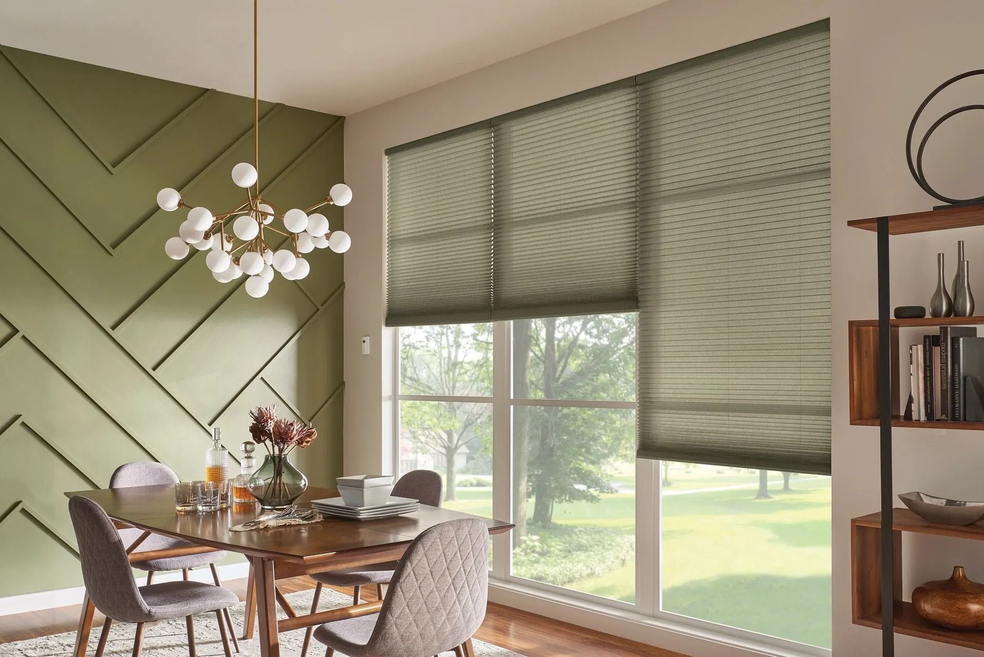 A modern dining room featuring a green geometric accent wall, a globe chandelier, and windows with pleated shades.