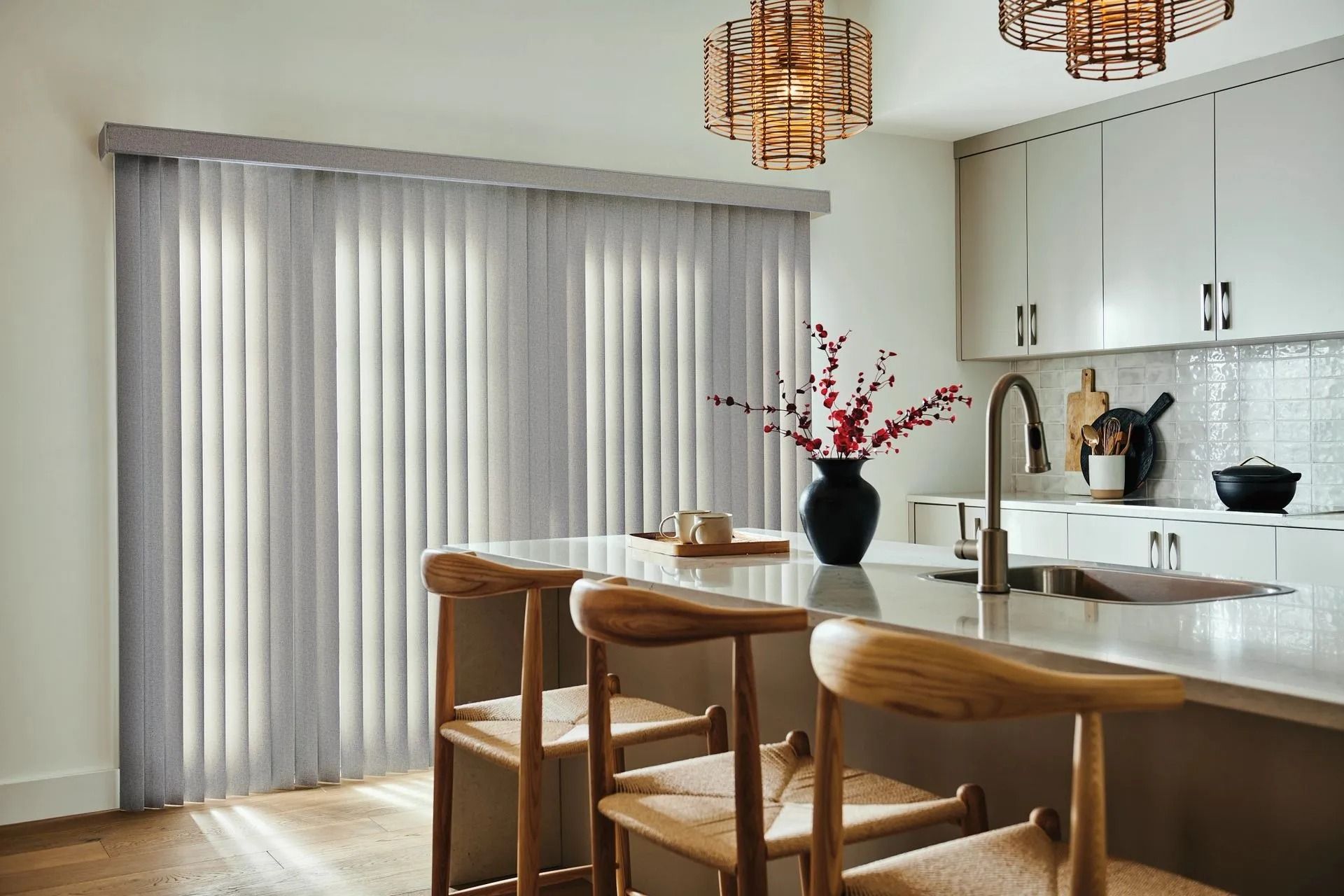 A kitchen island with two wooden stools sits before large, grey vertical blinds on a sliding door in a modern home.