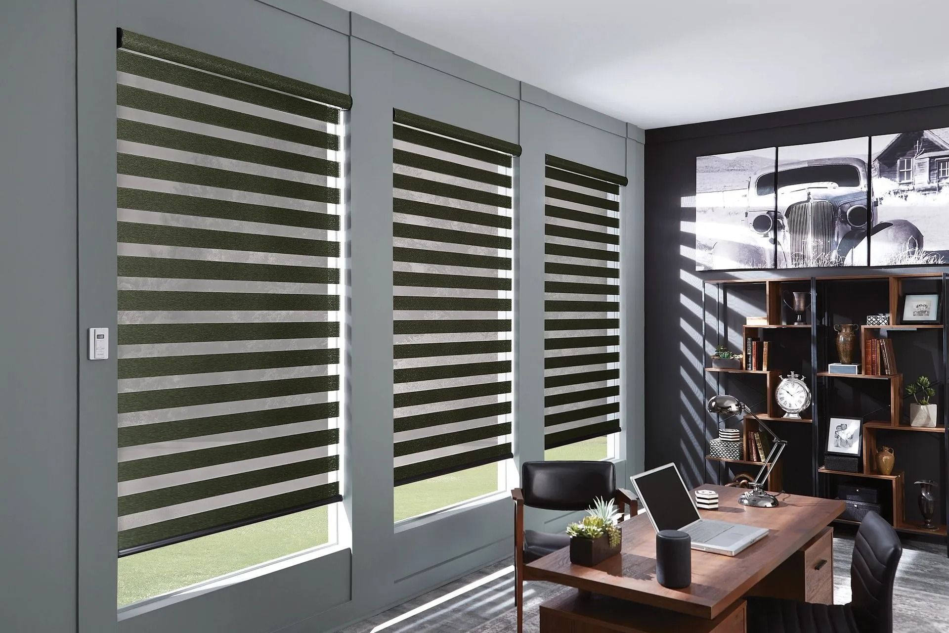 Modern home office featuring three windows with dark-striped roller shades, a wooden desk, and a wall art piece.