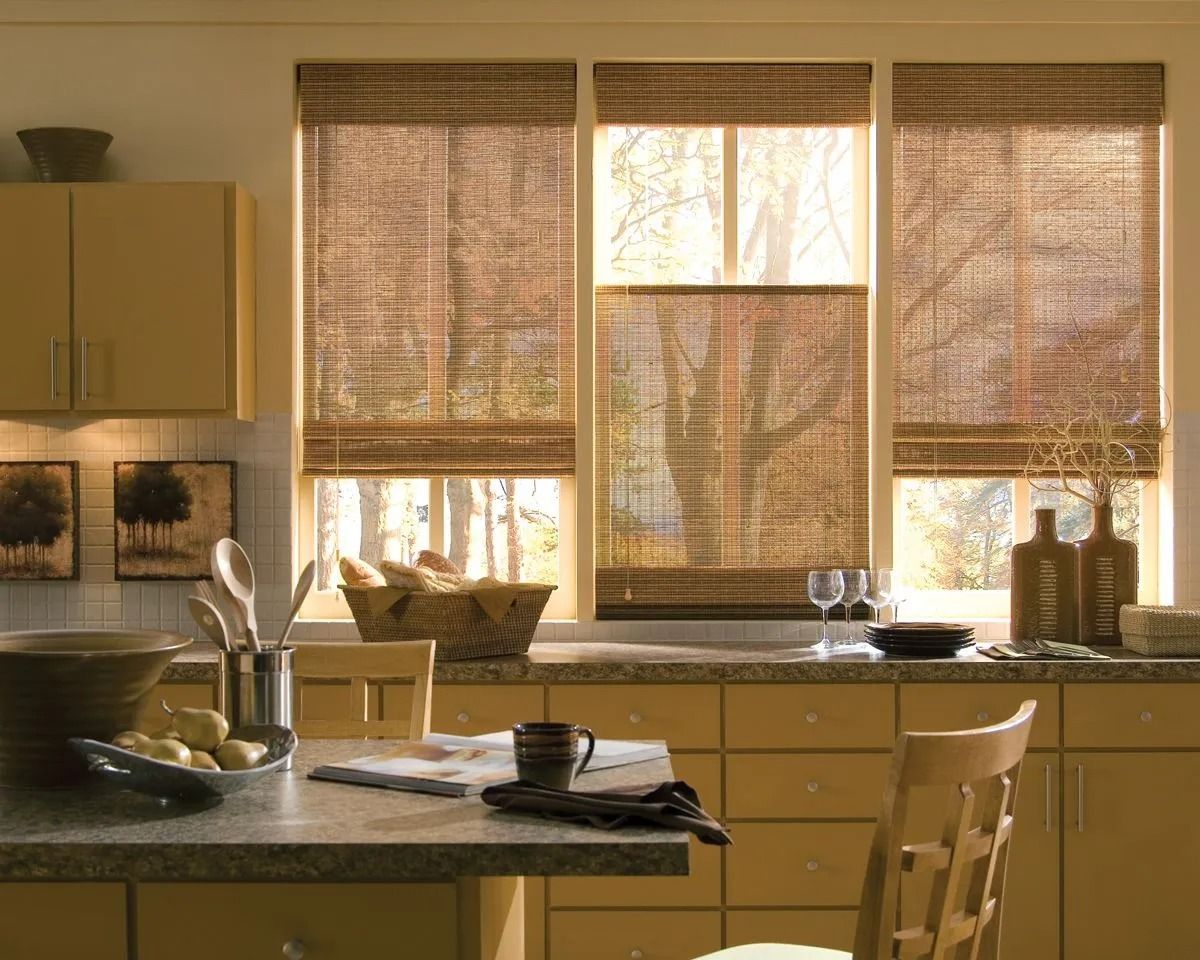 Three windows with adjustable bamboo shades in a warm-toned kitchen with countertops and wooden cabinetry.
