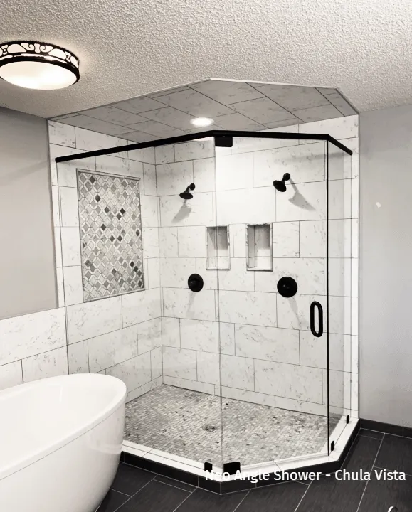 Black and white photo of a modern corner shower with glass doors, stone tile, and black fixtures.