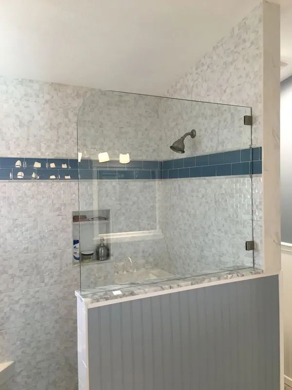 Glass shower enclosure with gray and white tile, blue accents, and a built-in shelf.