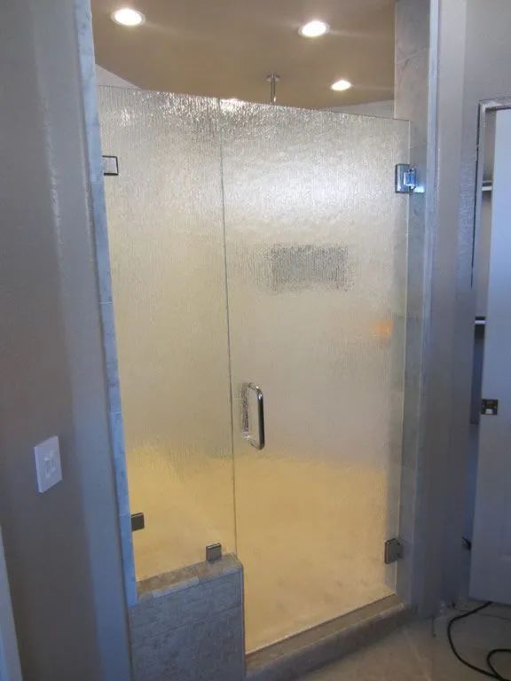 Frosted glass shower door in a modern bathroom. Chrome hardware and recessed lighting.