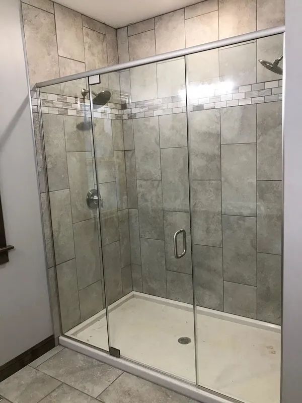 Glass shower enclosure with gray tiled walls and a white base. Silver shower fixtures.