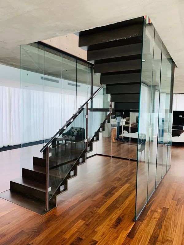 Modern staircase with glass walls and dark wood steps. Wooden floors reflect natural light.